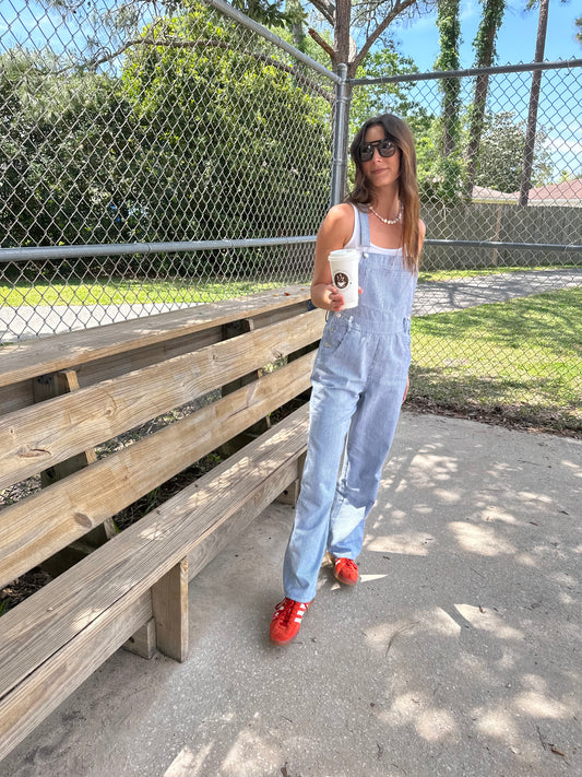 Girl in park wearing cute long overalls for women holding a coffee wearing adidas gazelles. 