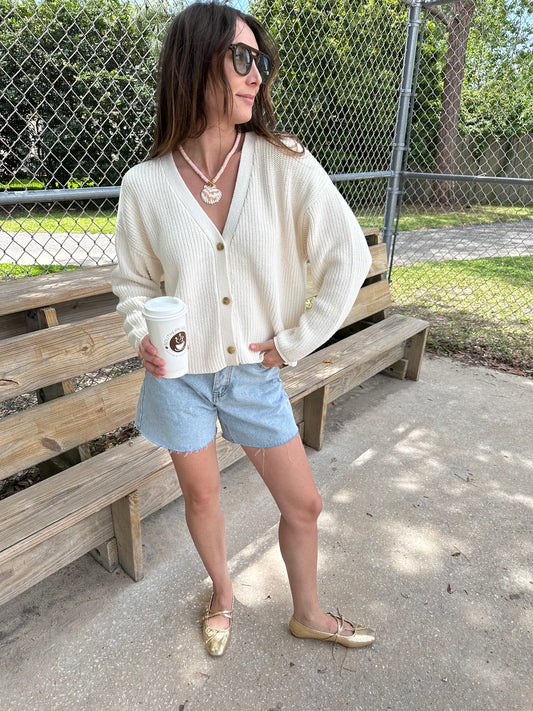 Woman wearing chunky cocoon cardigan, Ivory knit cardigan sweater and seashell necklace holding a coffee.