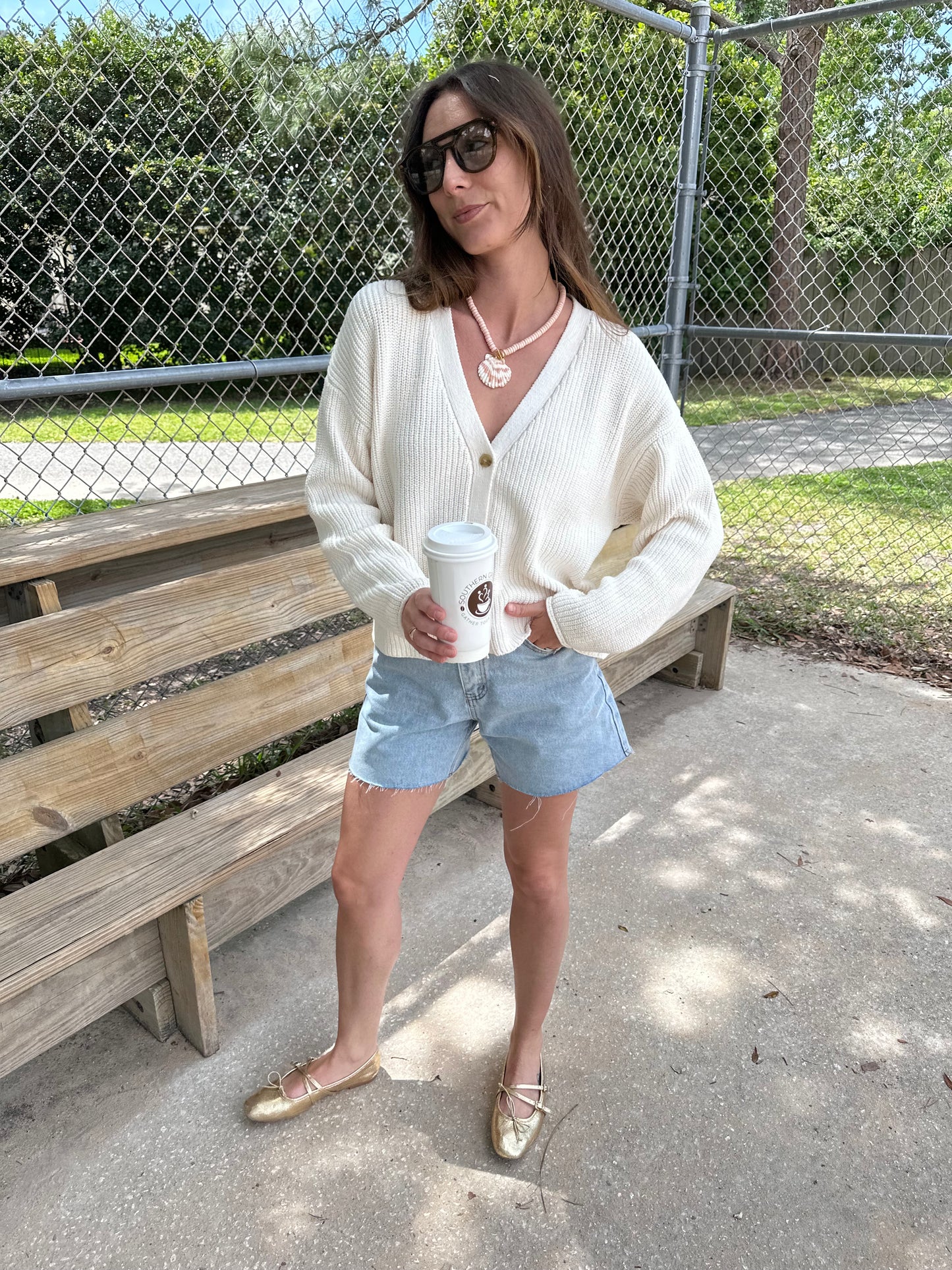 Woman wearing chunky cocoon cardigan, Ivory knit cardigan sweater and seashell necklace holding a coffee.