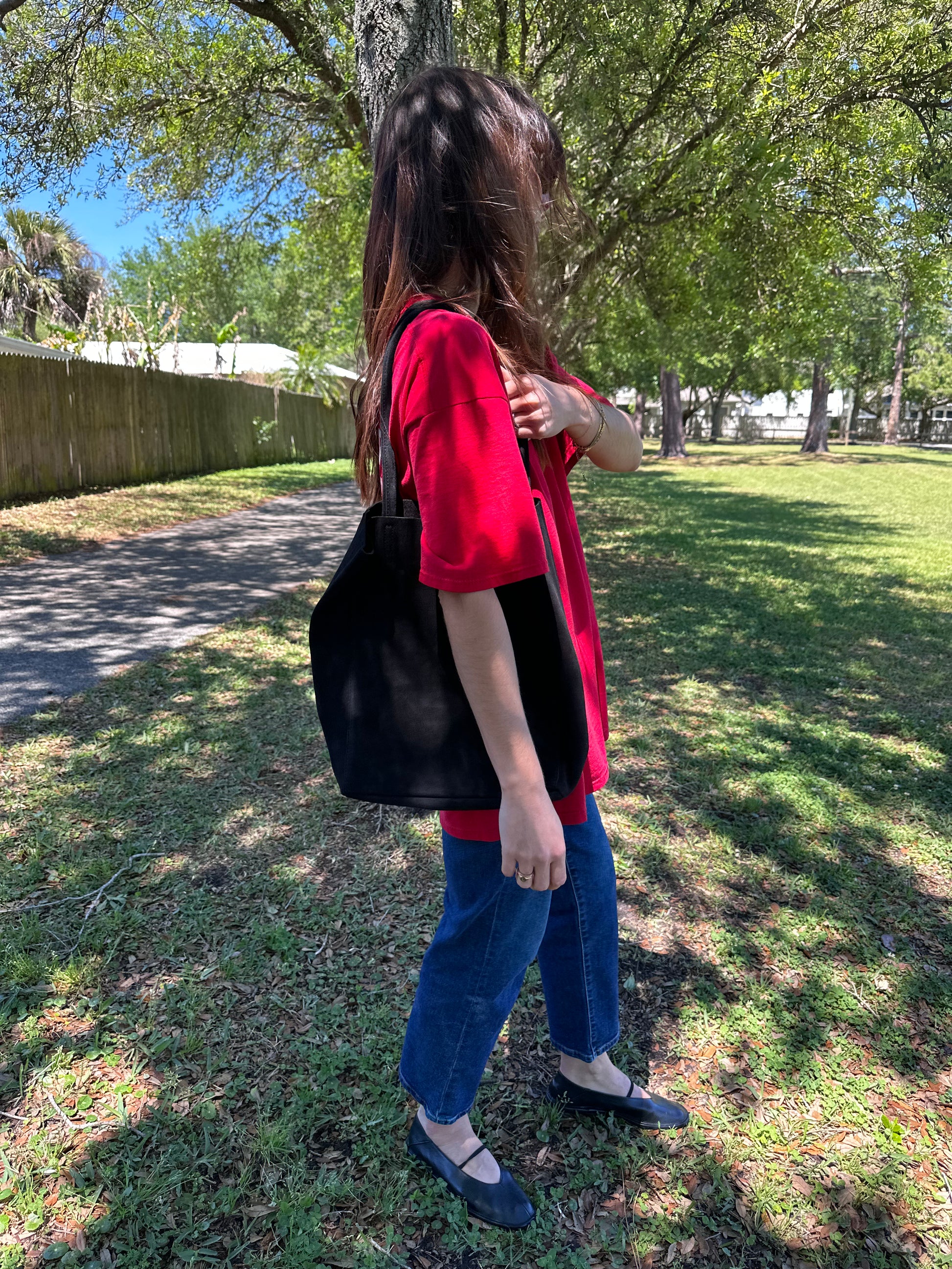 Girl holding black suede tote in park wearing vintage red graphic tee and vintage levi ribcage straight jeans in mid wash.