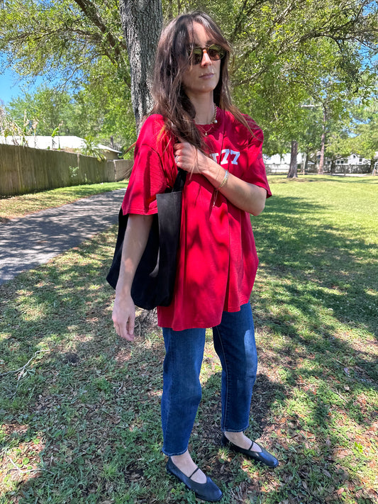 Girl holding black suede tote in park wearing vintage red graphic tee and vintage levi ribcage straight jeans in mid wash.