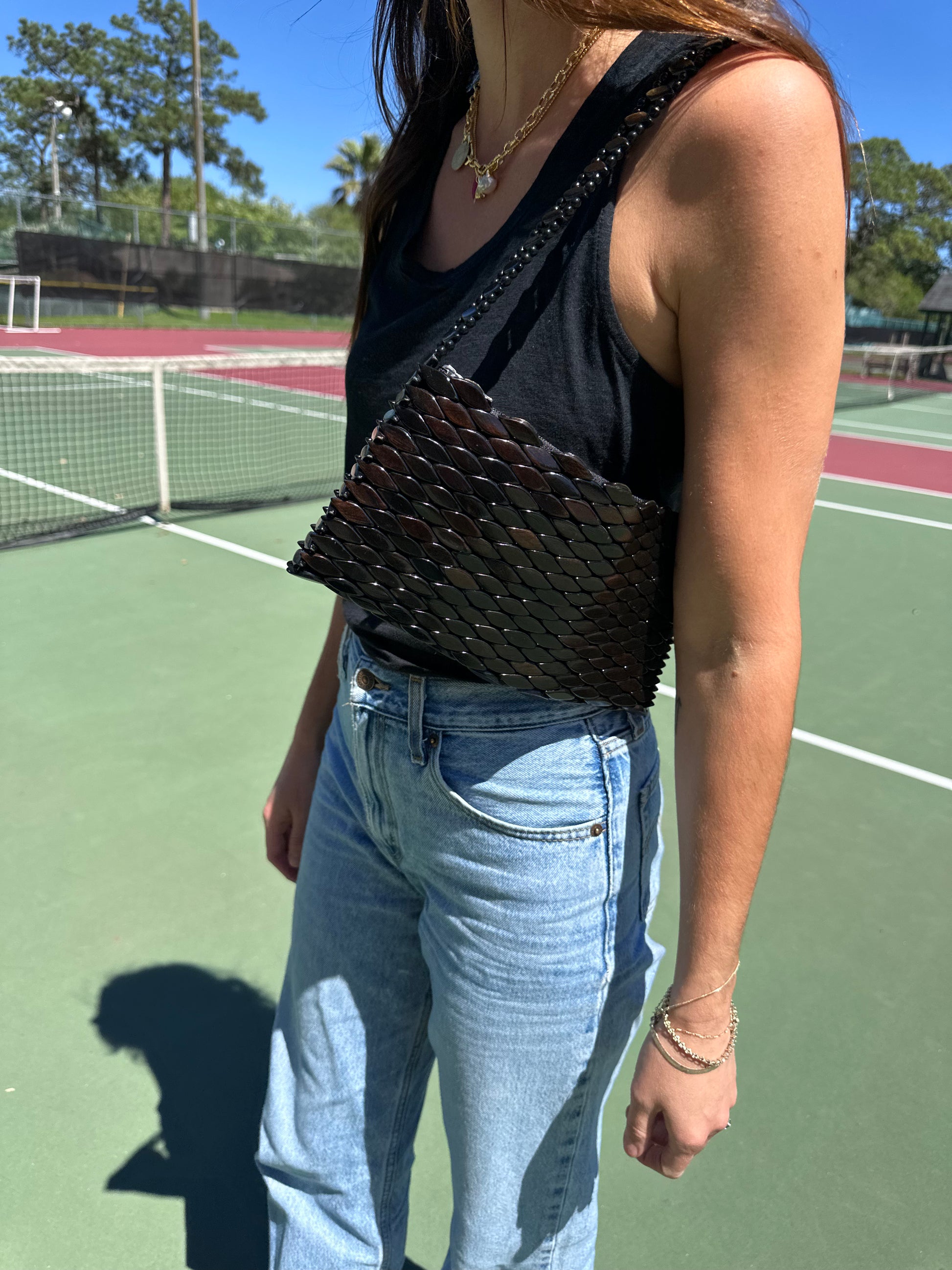 Woman in American Vintage Clothing tank top wearing gold charm necklace and vintage beaded shoulder bag. 